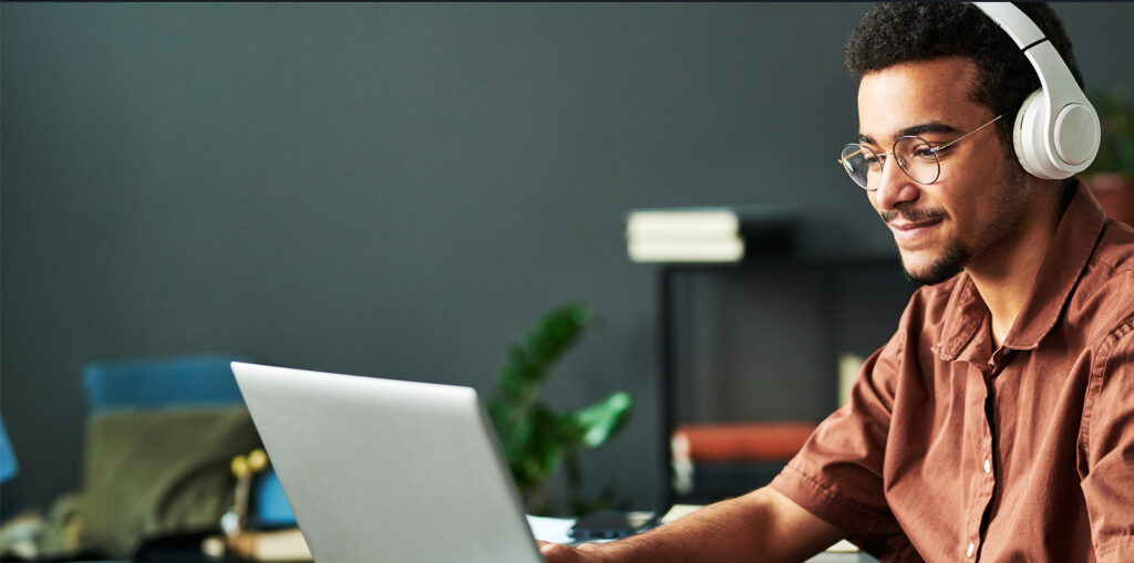 Young smiling man in headphones typing on laptop keyboard