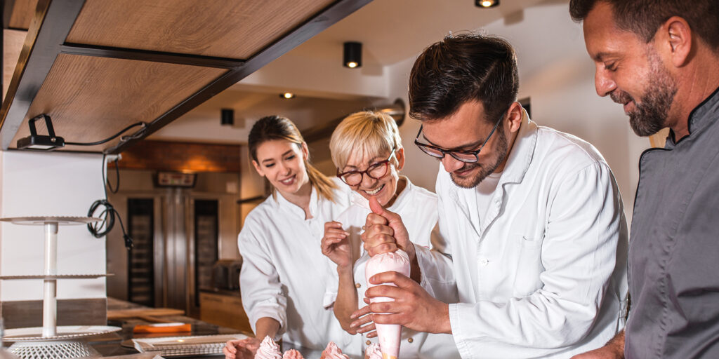 Group of workers in uniform decorating desserts in modern manufa