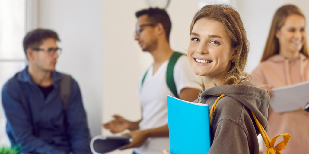 Portrait of happy university student girl holding her book and smiling at camera